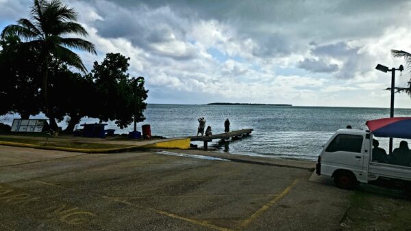 A dock with people standing on it and cars parked in front of the water.